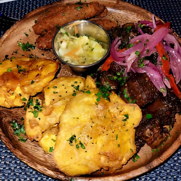 Haitian griot platter with fried plantains, pikliz, and fried pork on a wooden plate.