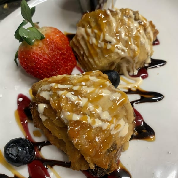 Two Haitian fried plantain fritters drizzled with sauce, served with a strawberry and blueberries.
