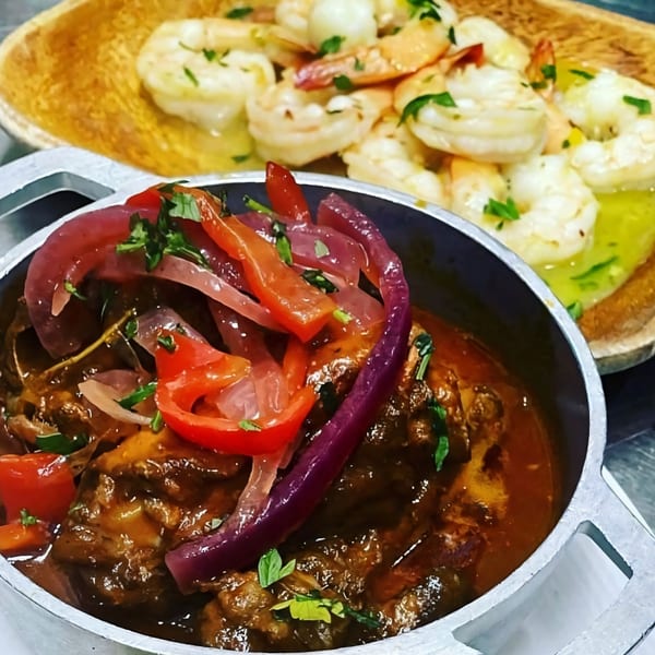 Haitian stew with red onions and peppers, alongside a wooden bowl of garlic shrimp.