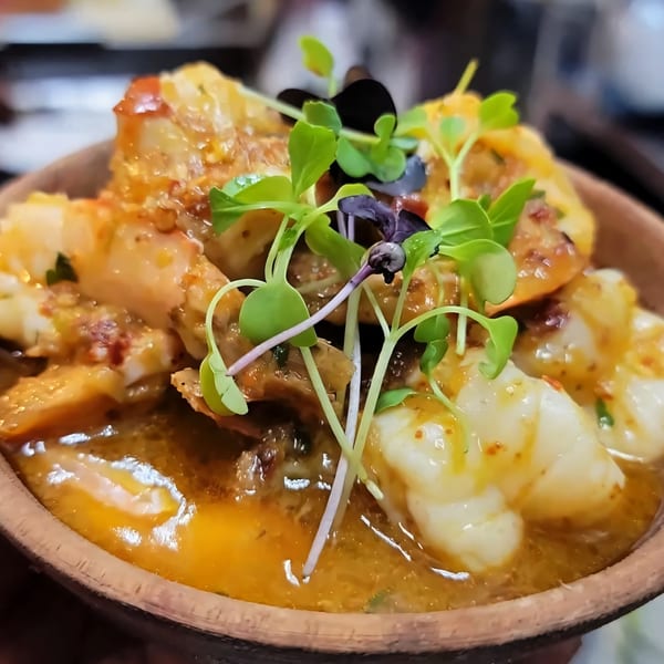 Haitian dish with shrimp or lobster in a rich orange sauce, garnished with fresh microgreens.
